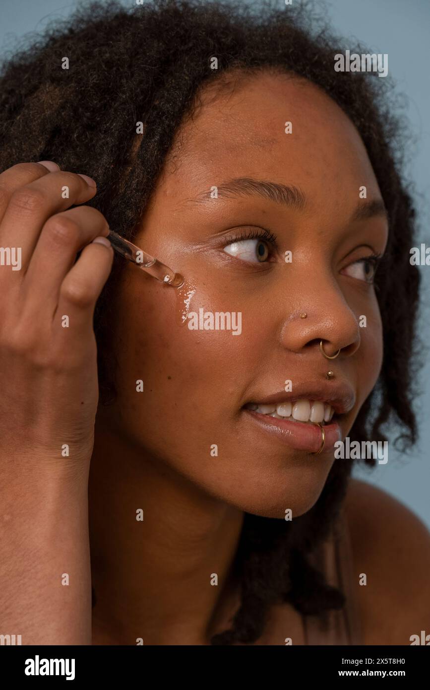 Giovane donna che applica siero sul viso Foto Stock