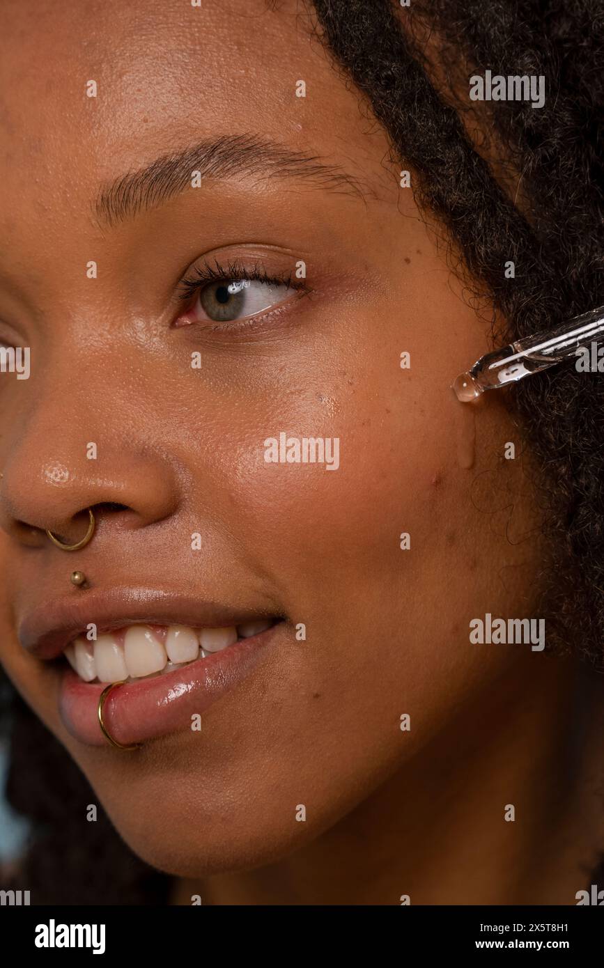 Giovane donna che applica siero sul viso Foto Stock