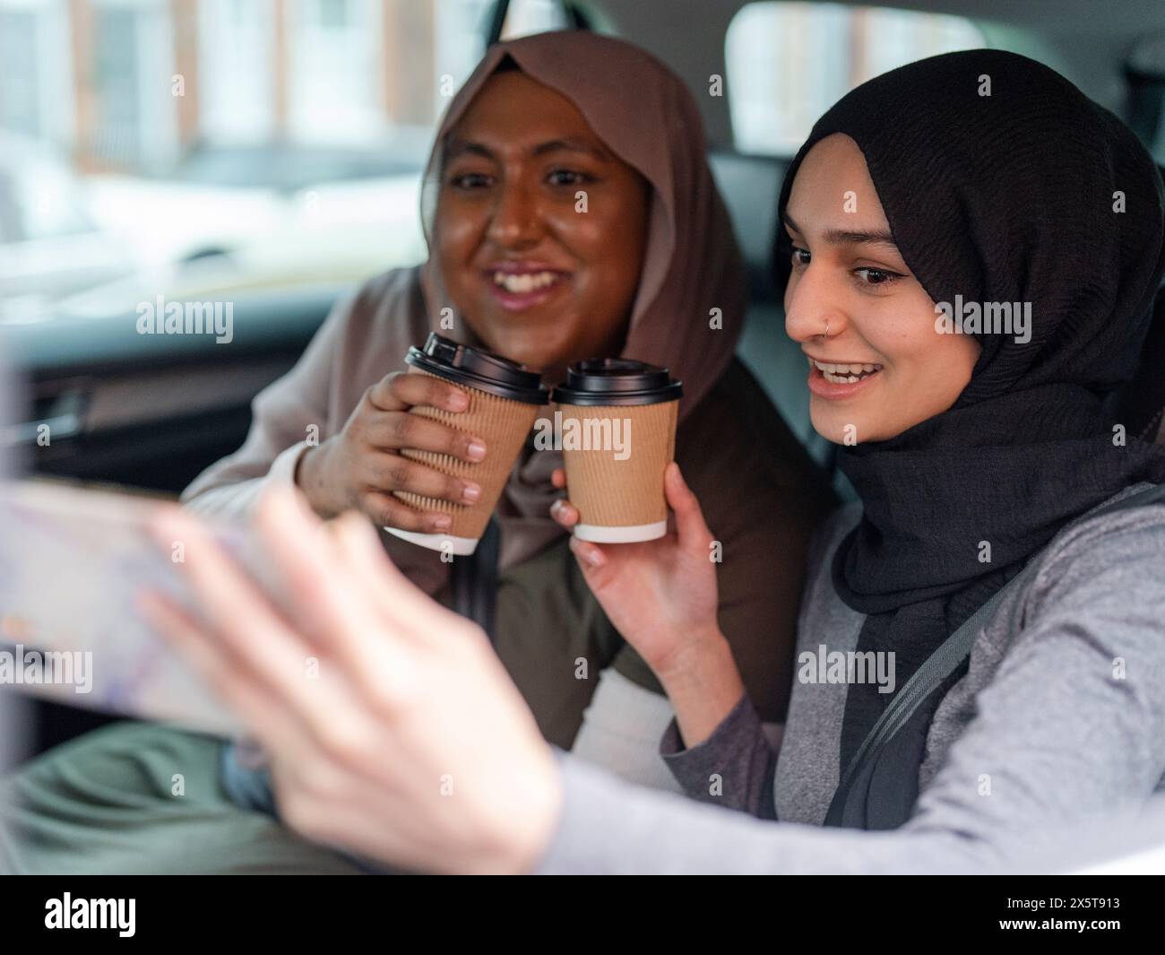 Donne allegre che bevono il caffè e si fanno selfie in auto Foto Stock