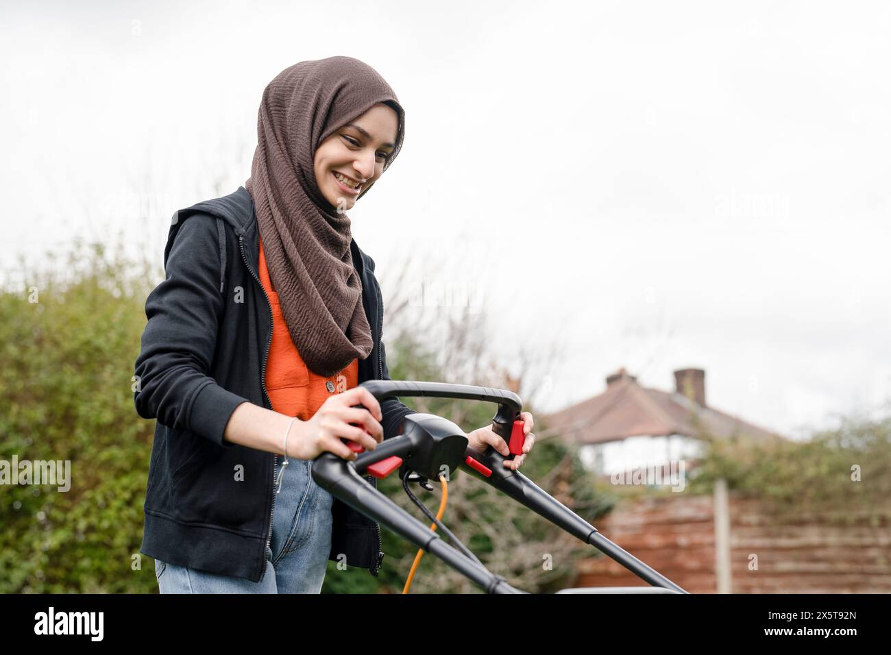 Donna che indossa l'hijab falciando l'erba nel cortile Foto Stock