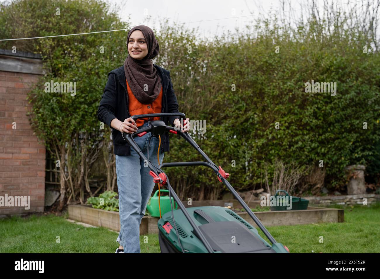 Donna che indossa l'hijab falciando l'erba nel cortile Foto Stock