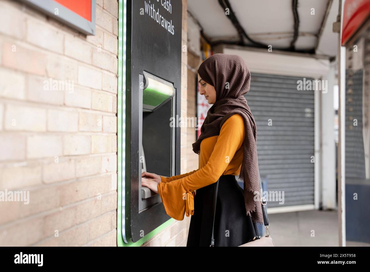 Donna in hijab che usa il bancomat Foto Stock