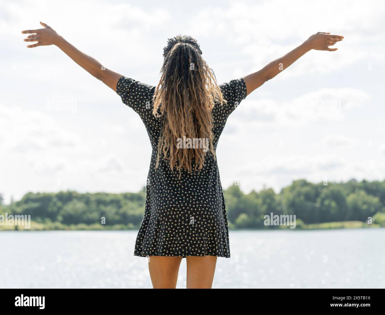 Donna in piedi con le braccia allungate dal lago nelle giornate di sole Foto Stock