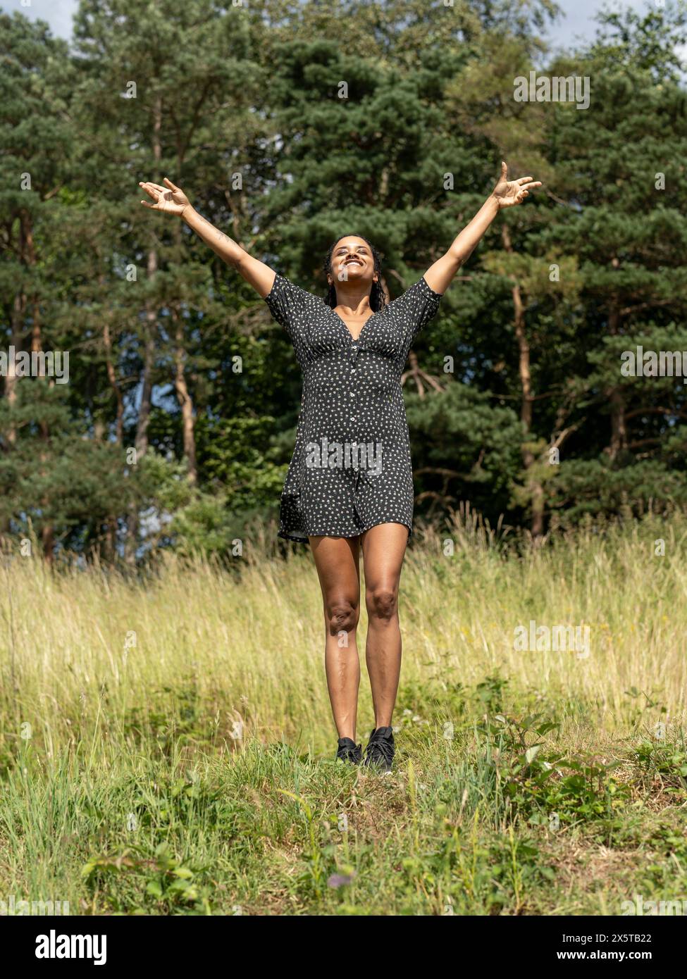 Donna in piedi con le braccia allungate sul prato nelle giornate di sole Foto Stock