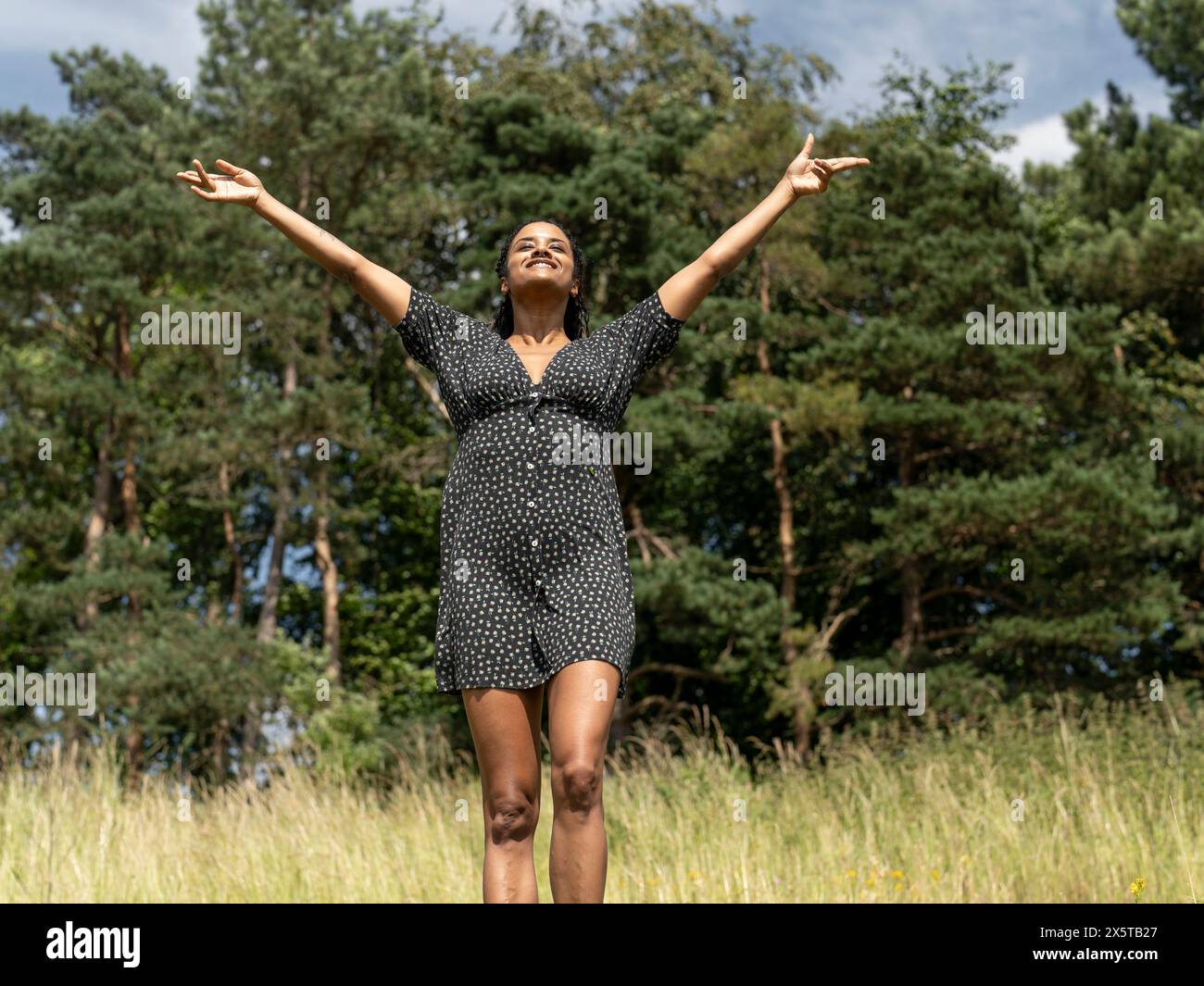 Donna in piedi con le braccia allungate sul prato nelle giornate di sole Foto Stock