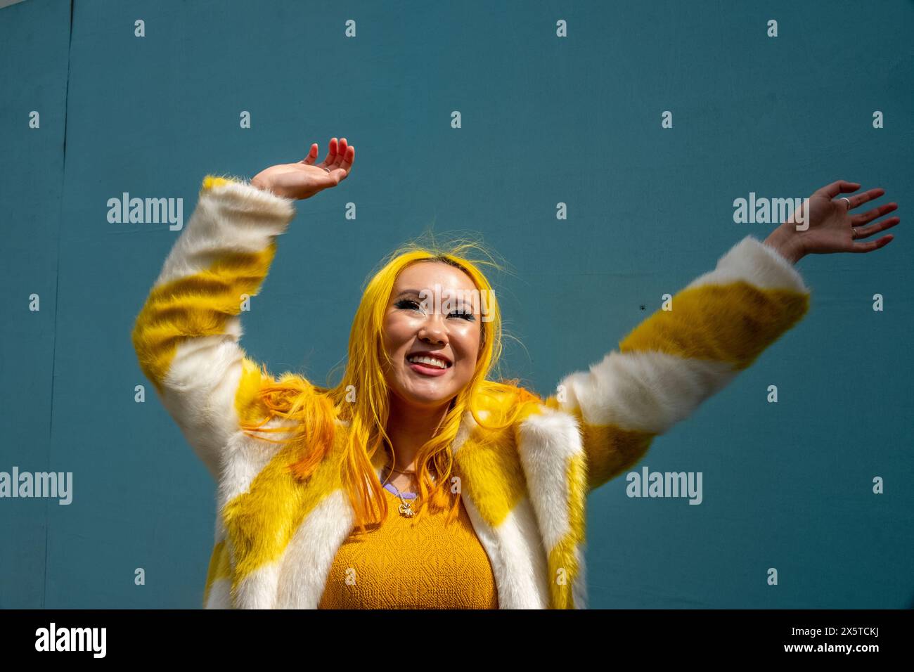 Giovane donna sorridente con capelli gialli che ondeggiano le braccia all'aperto Foto Stock