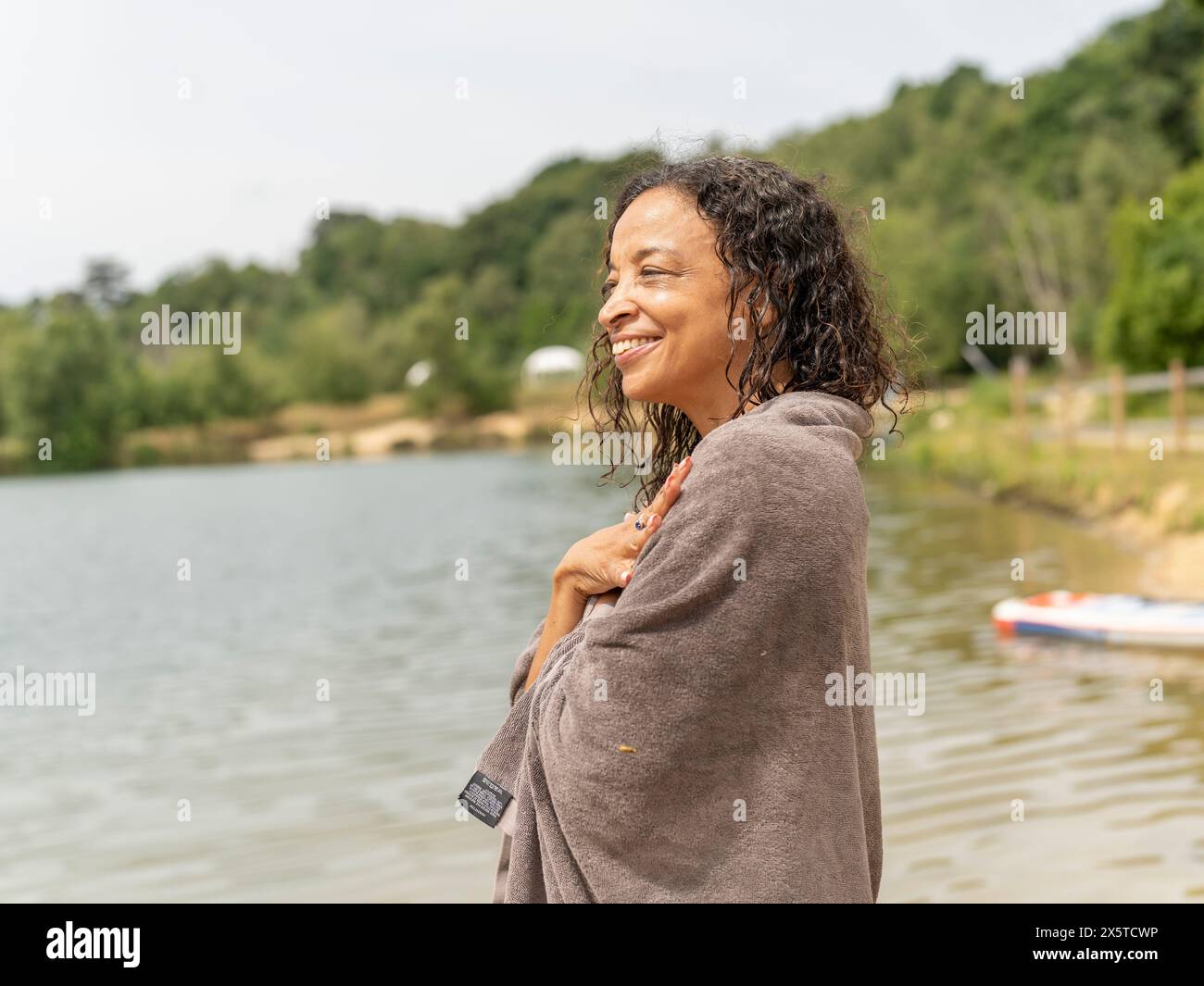 Donna sorridente avvolta in un asciugamano in piedi sul lago Foto Stock
