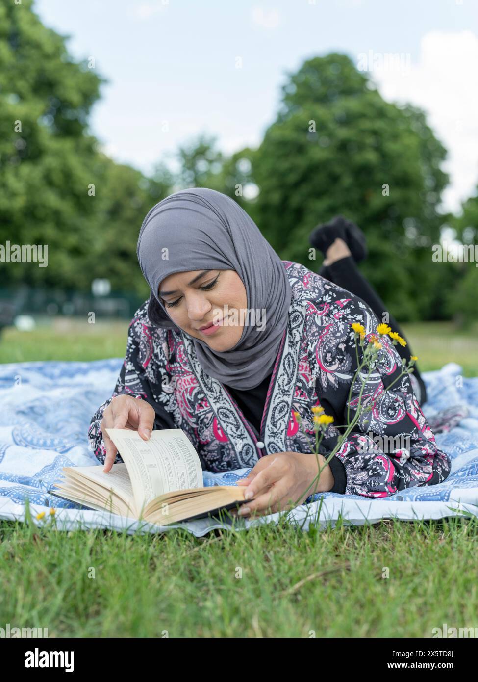 Regno Unito, Sutton, donna con il velo che legge un libro sul prato nel parco Foto Stock