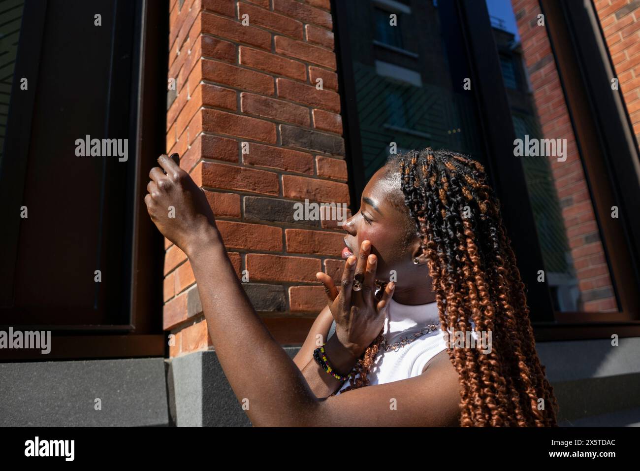 Donna che tiene un piccolo specchio e applica il prodotto di bellezza sul viso Foto Stock