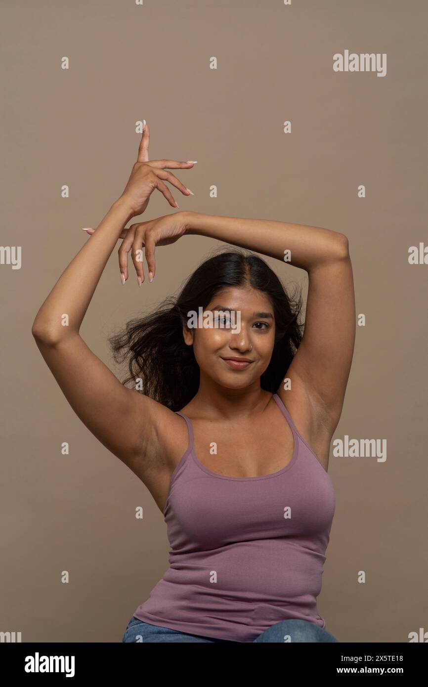 Ritratto in studio di una donna sorridente con la parte superiore viola e le braccia sollevate Foto Stock