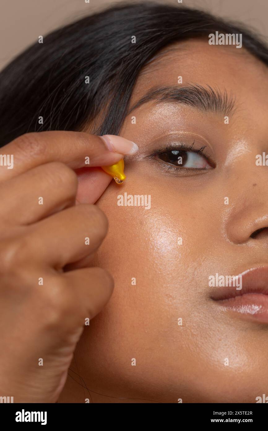 Primo piano di una donna che fa cadere il siero cutaneo sul viso Foto Stock