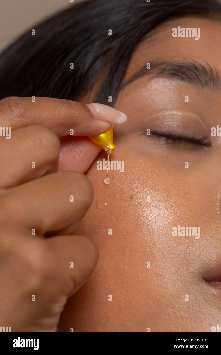 Primo piano di una donna che fa cadere il siero cutaneo sul viso Foto Stock