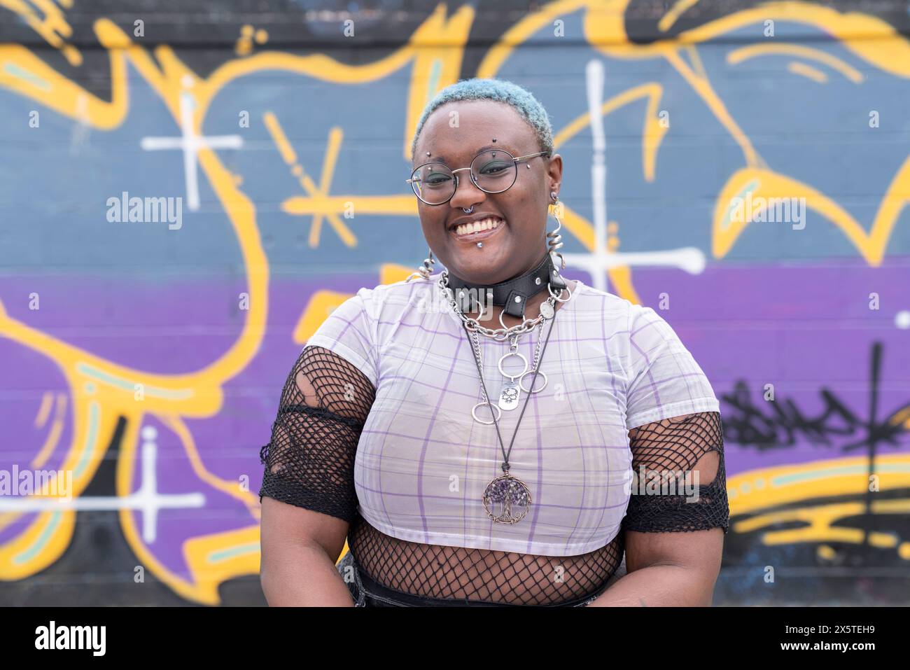 Ritratto di una persona sorridente non binaria contro il muro dei graffiti Foto Stock