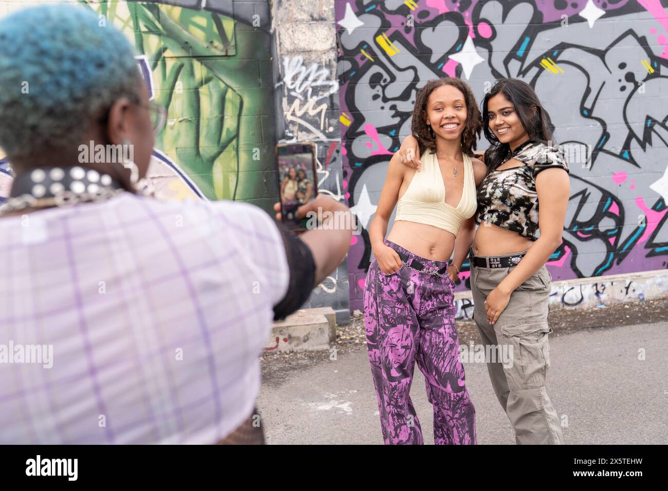 Persona non binaria che fotografa gli amici contro il muro dei graffiti Foto Stock