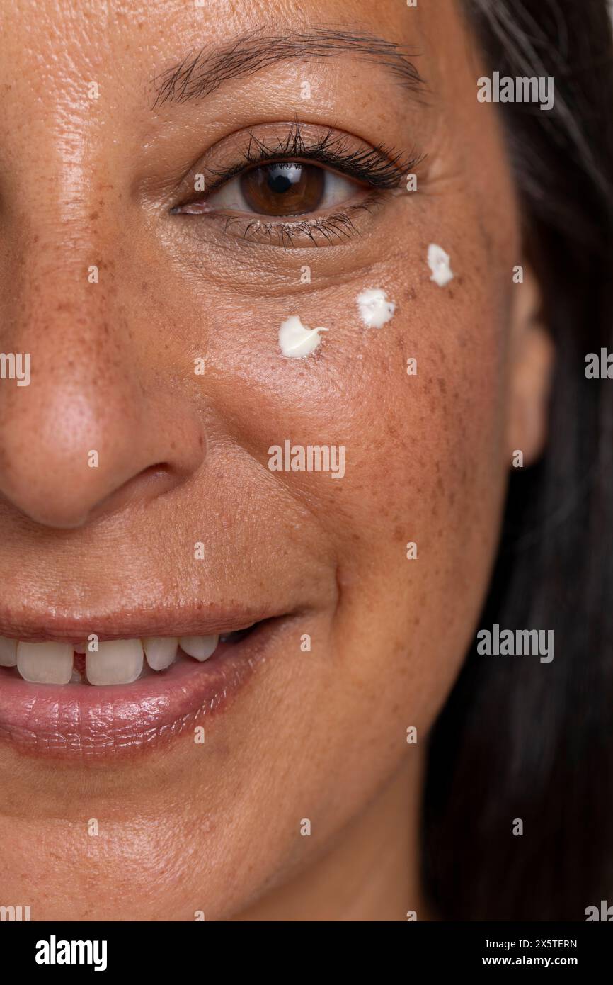 Primo piano di donna sorridente con puntini di crema per gli occhi Foto Stock