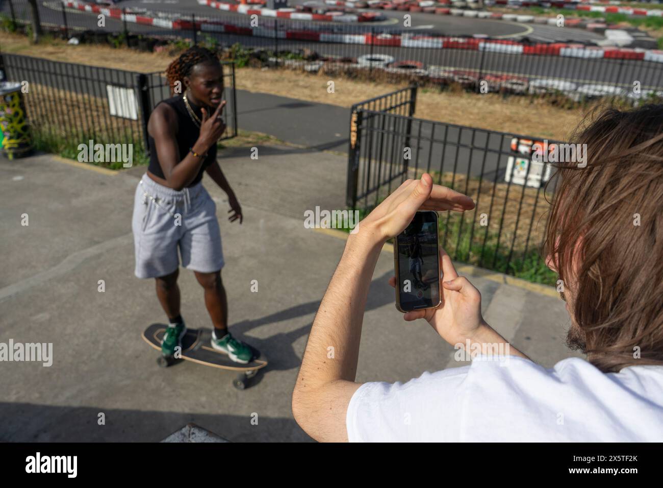Uomo che fotografa un'amica donna sullo skateboard Foto Stock