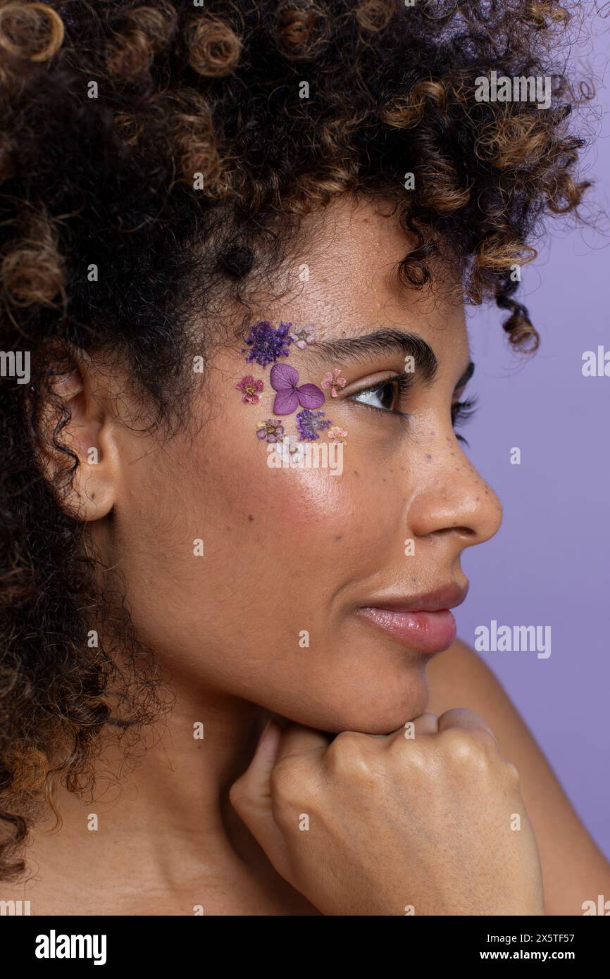 Vista laterale della donna bruna con fiori sul viso Foto Stock