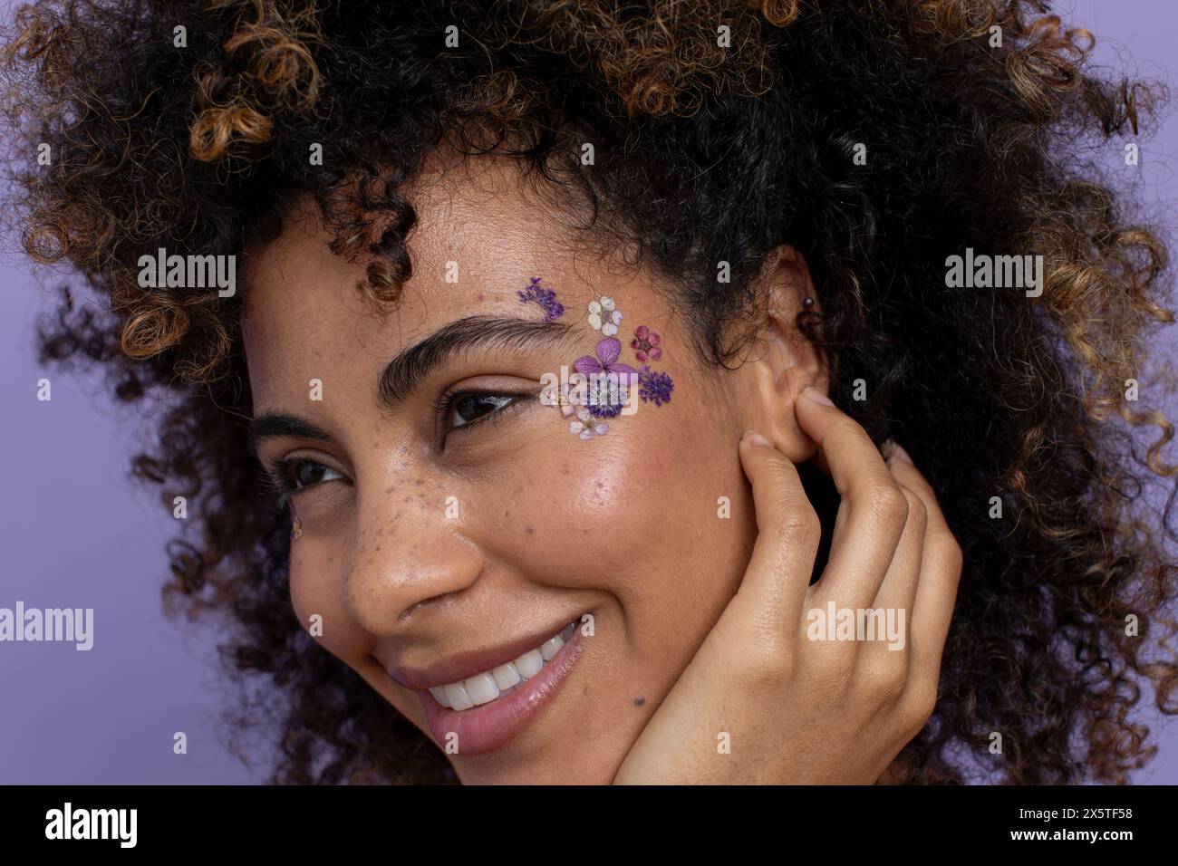 Donna sorridente con fiori attaccati in faccia Foto Stock