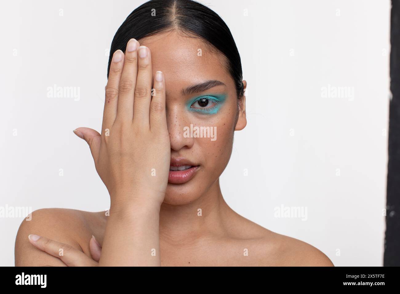 Donna che indossa il trucco blu, che protegge parte del viso con la mano Foto Stock