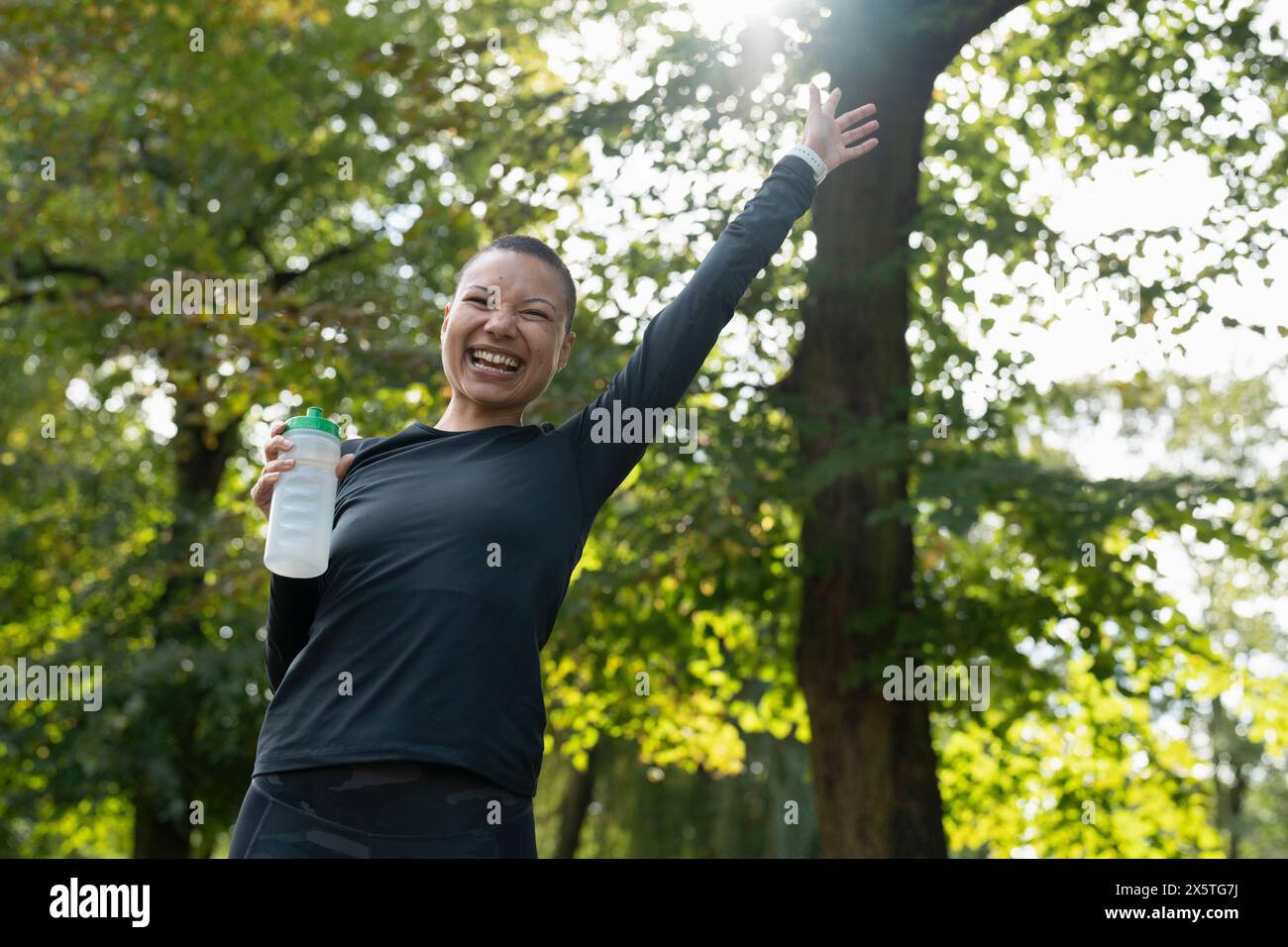 Ritratto di una donna atletica sorridente con il braccio sollevato nel parco Foto Stock