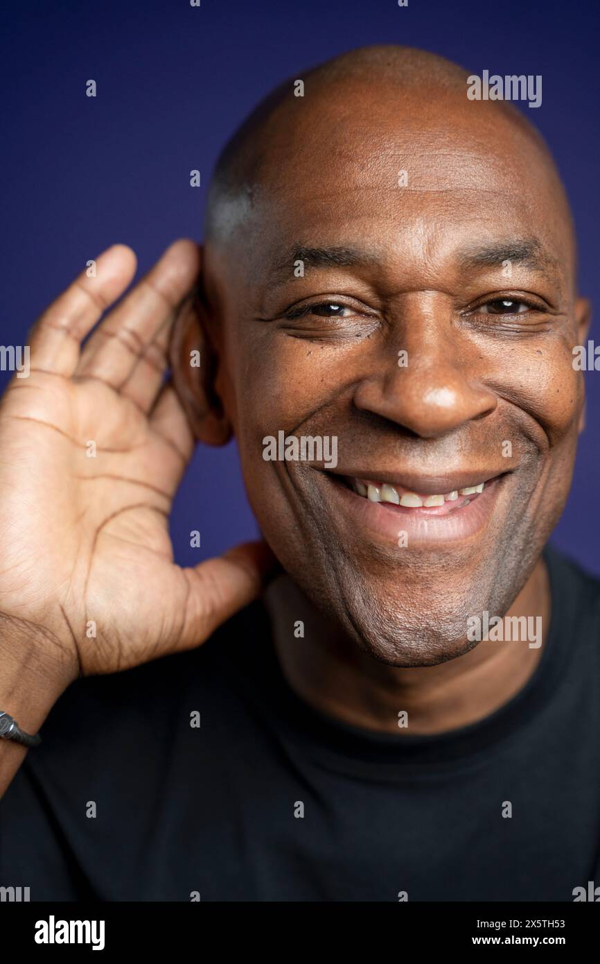 Ritratto dell'uomo sorridente con mano sull'orecchio su sfondo viola Foto Stock