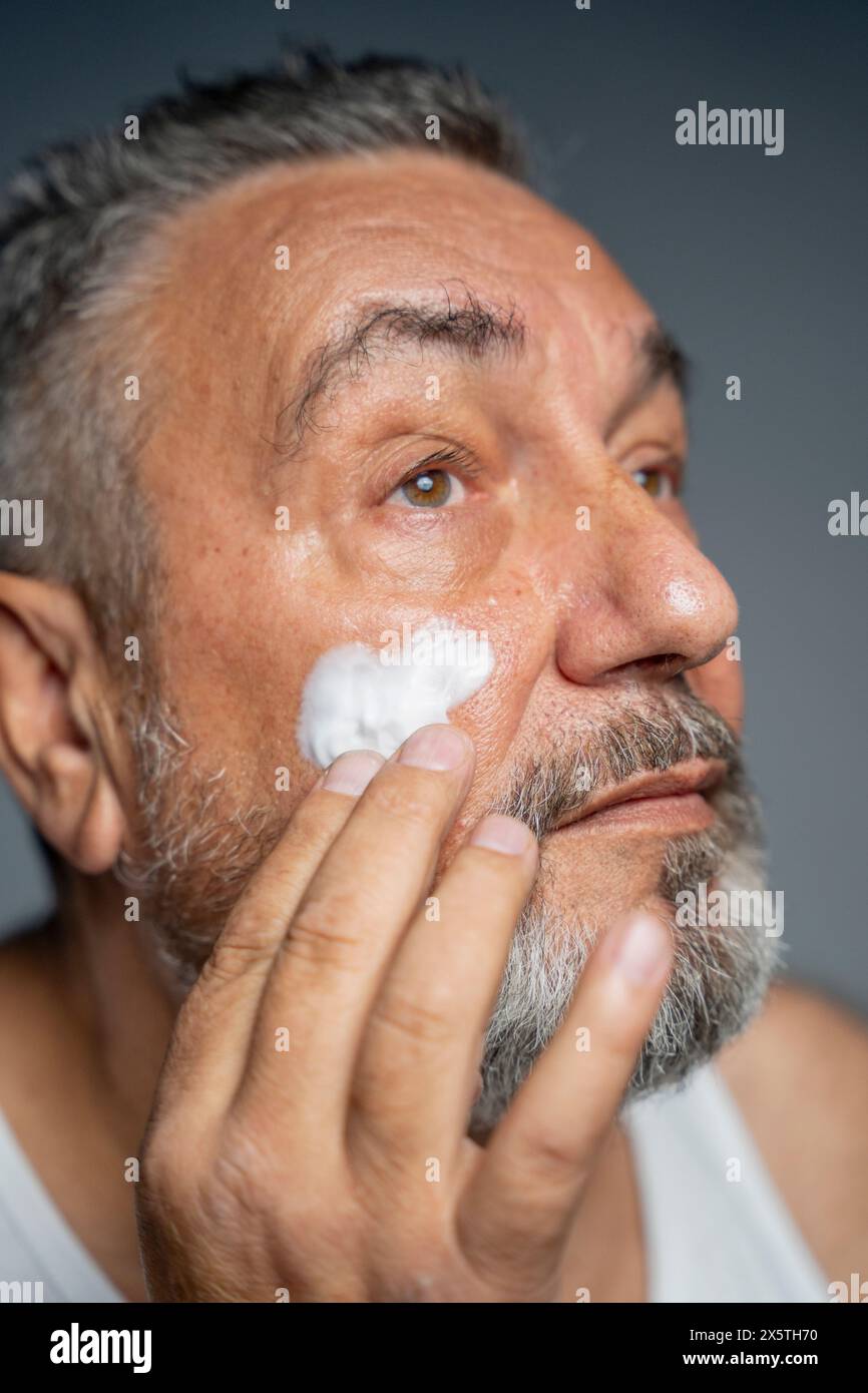 Ritratto dell'uomo che applica la crema sul viso Foto Stock