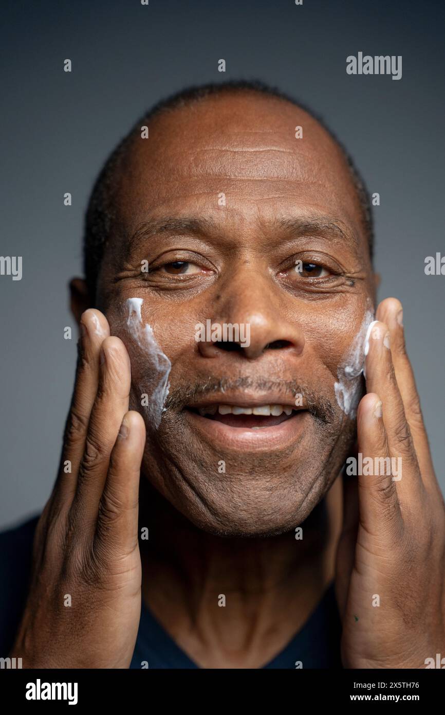 Ritratto dell'uomo che applica la crema sul viso Foto Stock