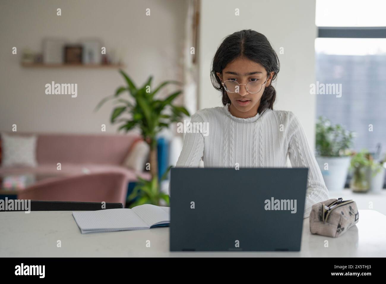 Ragazza che fa i compiti e usa un computer portatile in salotto Foto Stock