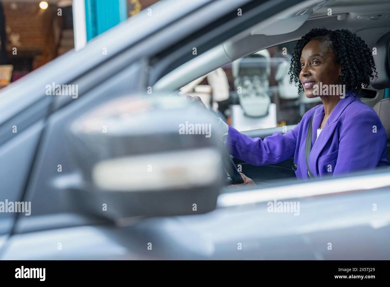 Donna elegante in giacca viola che guida un'auto Foto Stock
