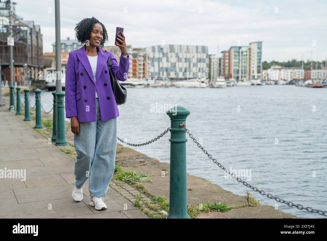 Donna sorridente che fotografa la vista della città con uno smartphone durante la passeggiata Foto Stock