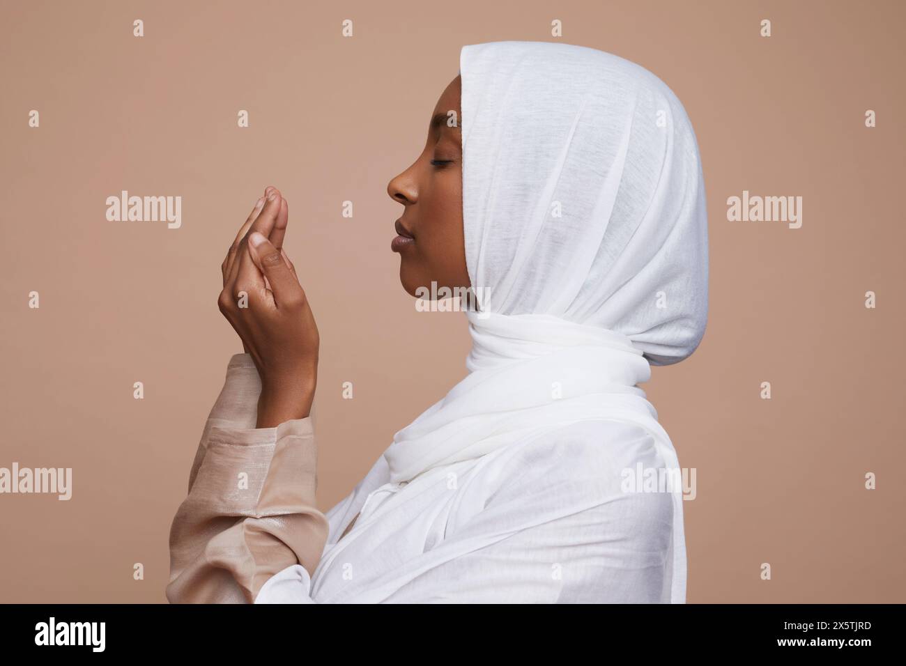 Foto di studio di una giovane donna in hijab bianco che prega Foto Stock