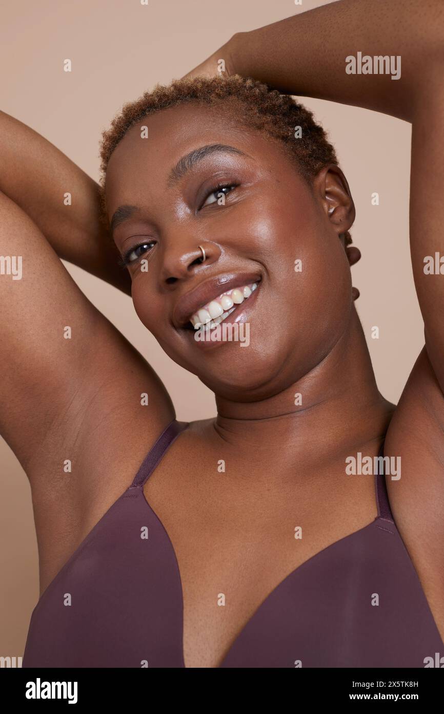 Ritratto in studio di una donna sorridente con le braccia sollevate e il reggiseno Foto Stock