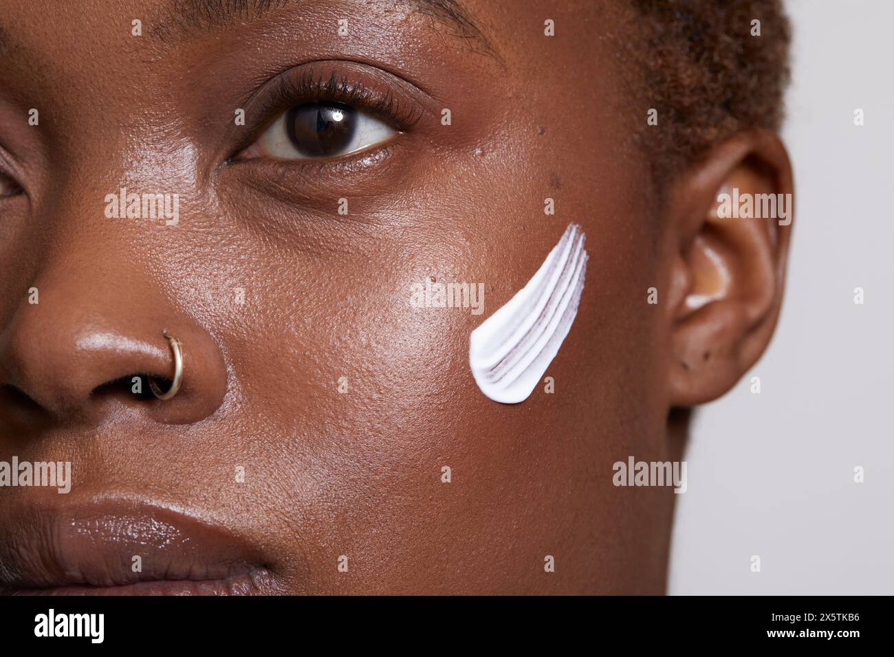Primo piano di una donna con crema per il viso sulla guancia Foto Stock