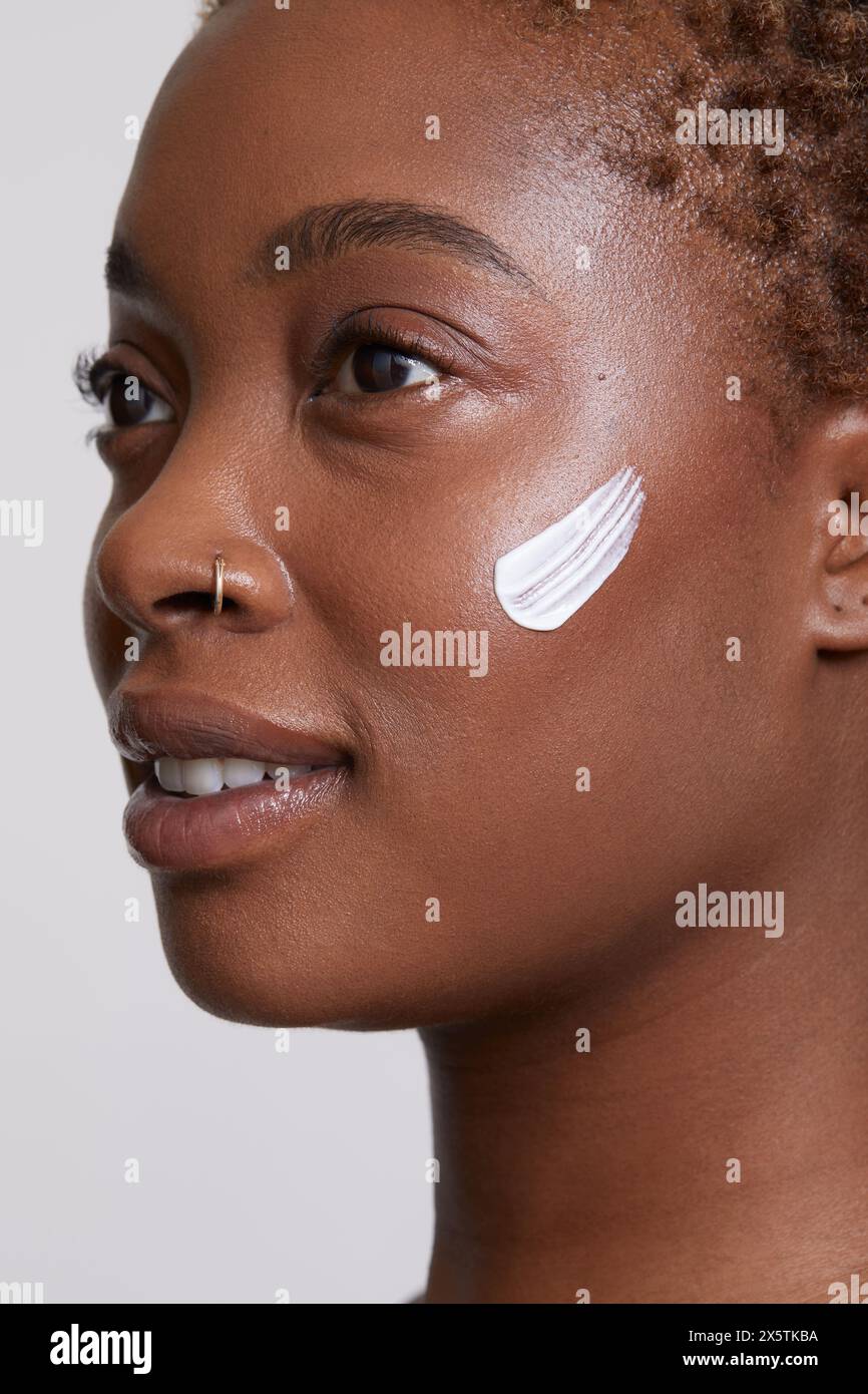 Primo piano di donna sorridente con crema per il viso sulla guancia Foto Stock