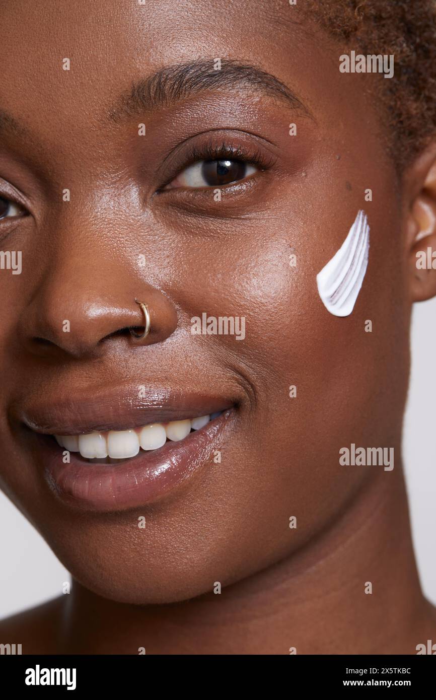 Primo piano di donna sorridente con crema per il viso sulla guancia Foto Stock