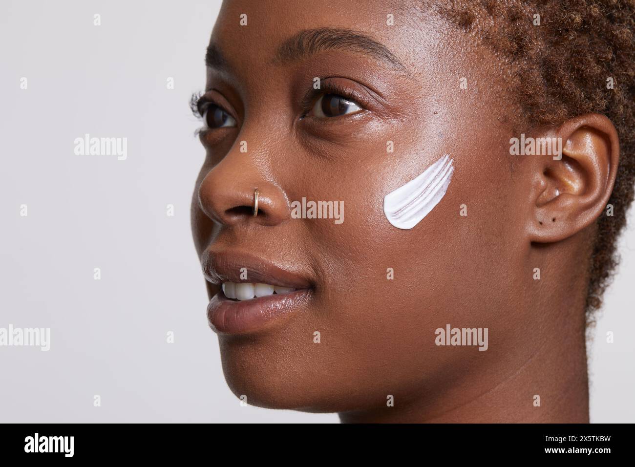 Primo piano di donna sorridente con crema per il viso sulla guancia Foto Stock