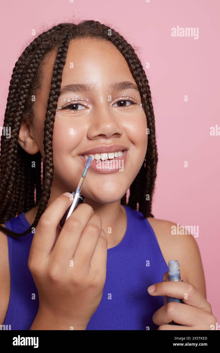 Ritratto in studio di una ragazza con adesivi decorativi sul viso che tengono il lucidalabbra Foto Stock