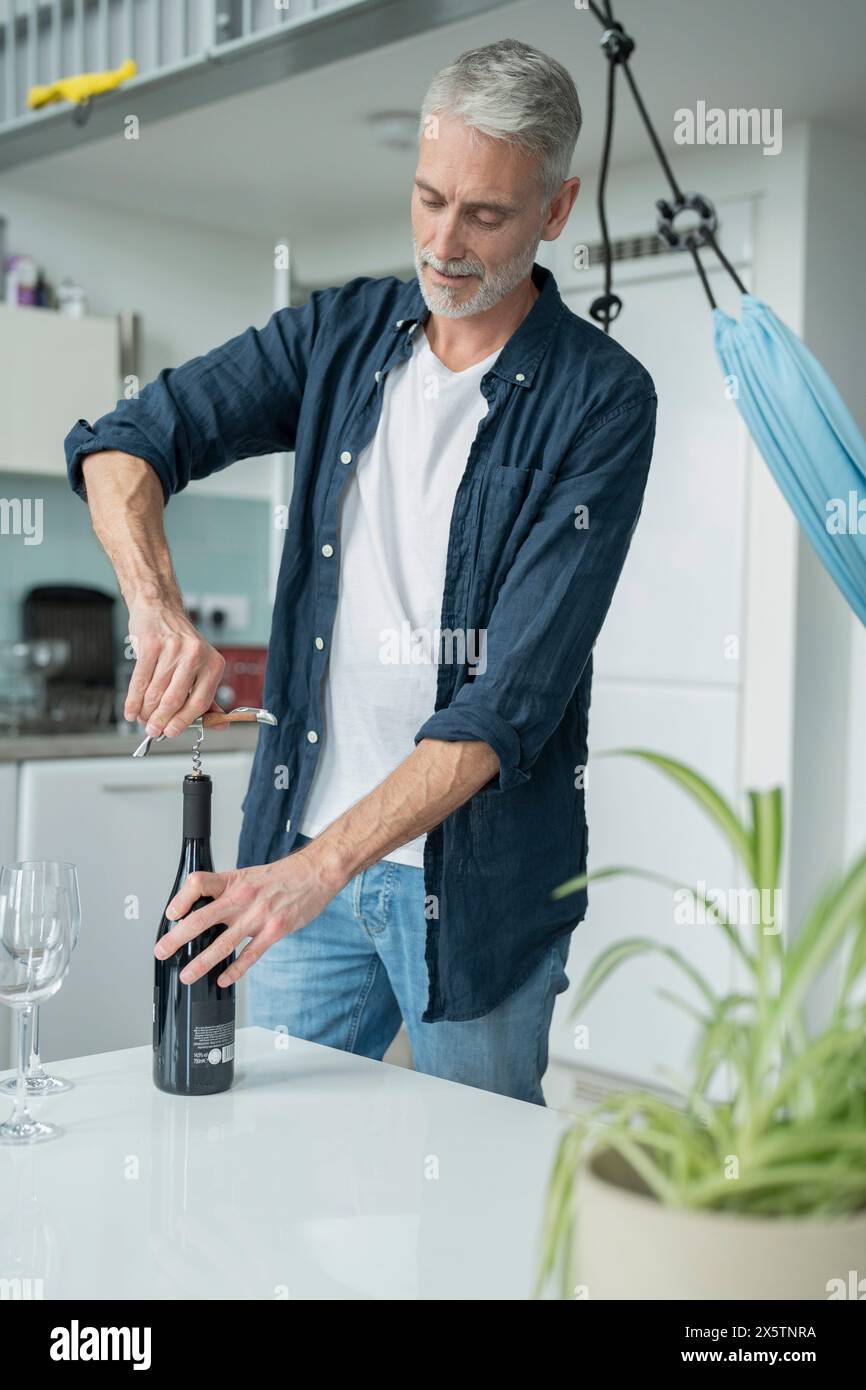 Uomo maturo che apre vino rosso a casa Foto Stock