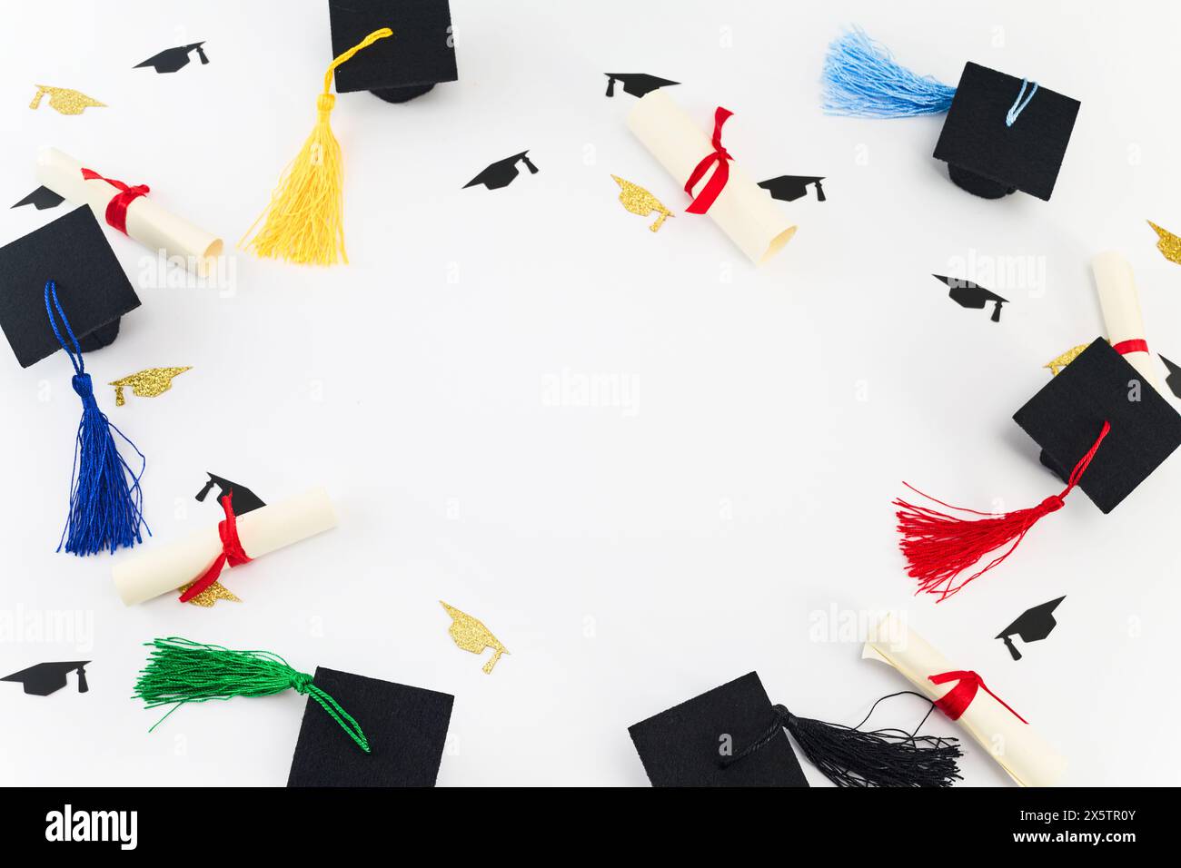 Tema per la cerimonia di laurea. Vista dall'alto dei berretti graduati in miniatura e dei diplomi con nappine colorate su bianco. Foto Stock