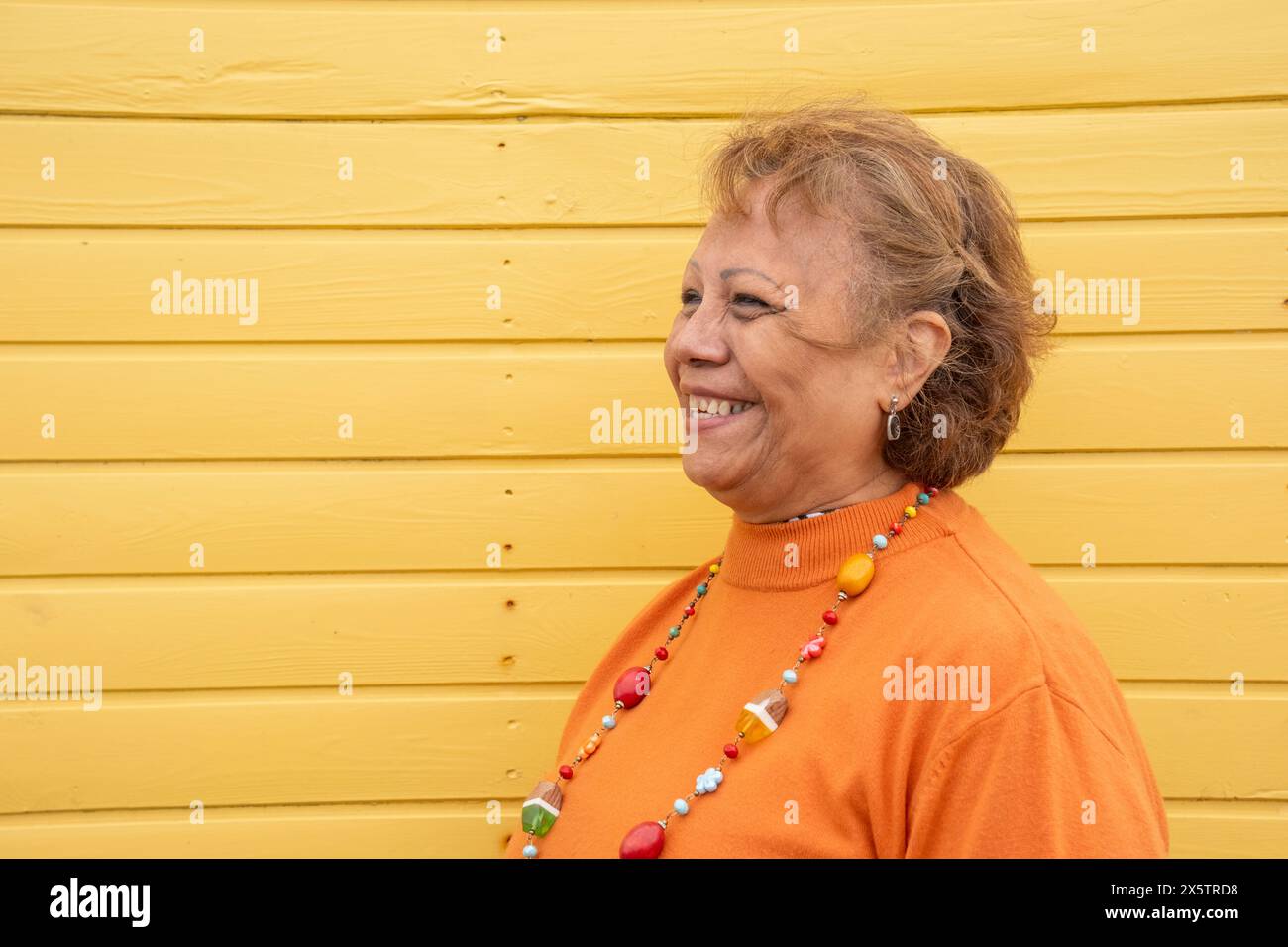 Ritratto di donna anziana sorridente contro il muro giallo Foto Stock