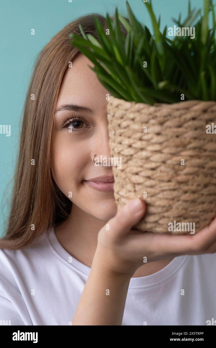 Primo piano di una ragazza adolescente che tiene una pianta in vaso davanti al viso Foto Stock