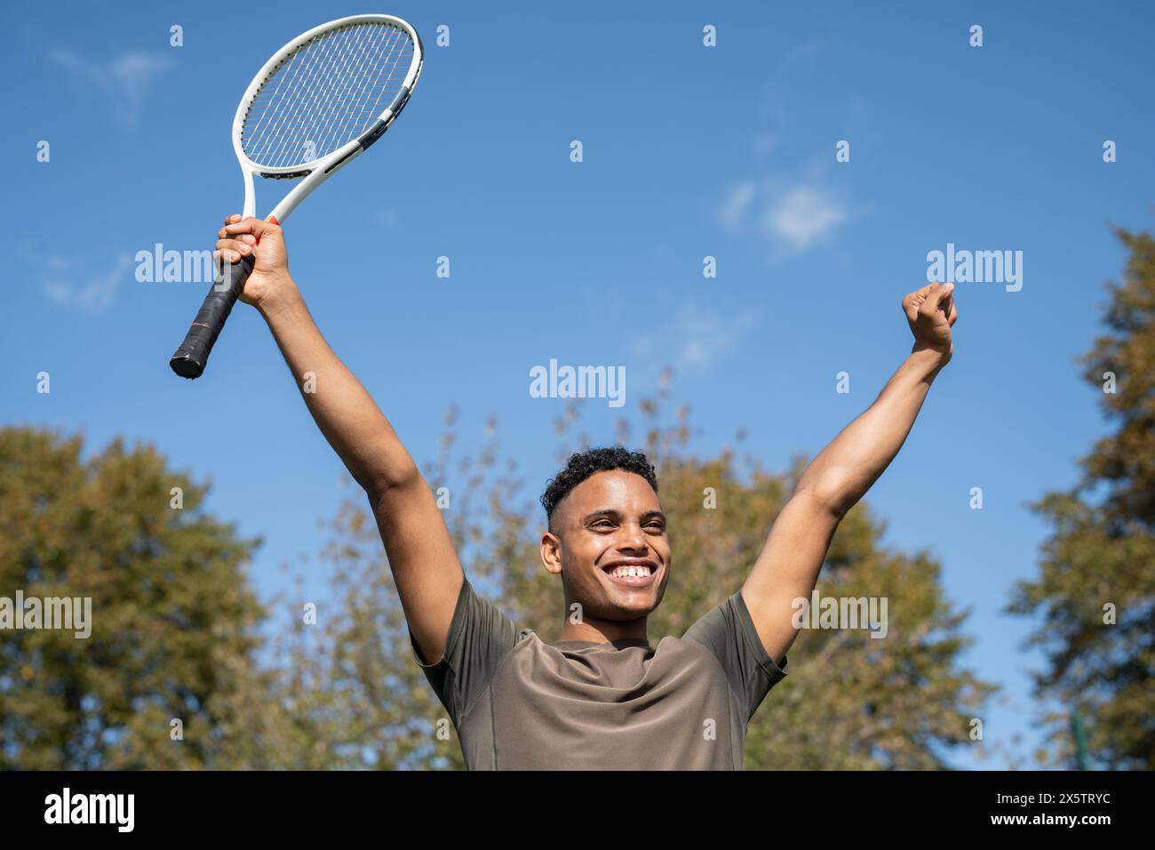 Uomo sorridente che alza le braccia con la racchetta da tennis Foto Stock