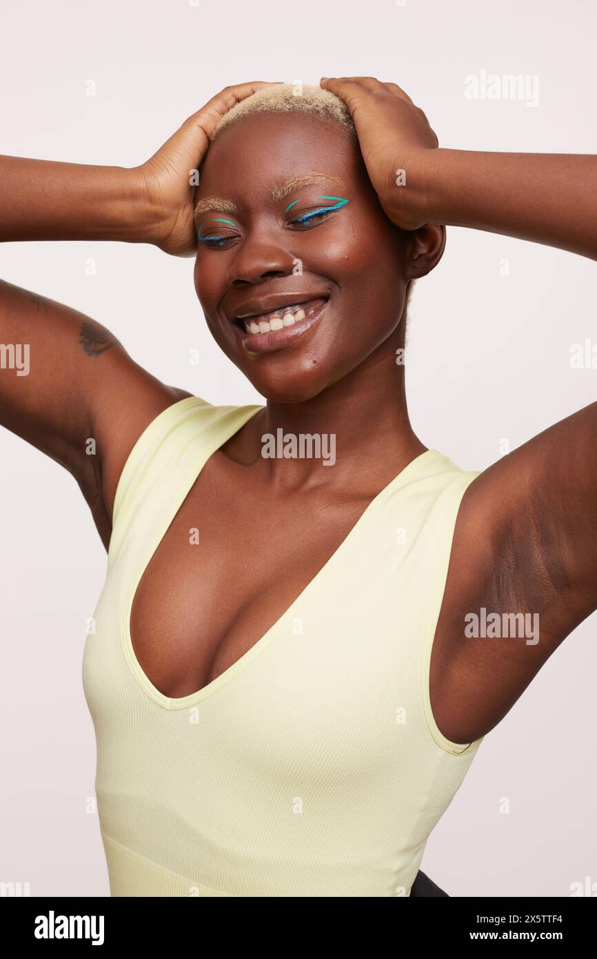 Donna sorridente con capelli bianchi corti, che tiene le mani sulla testa Foto Stock