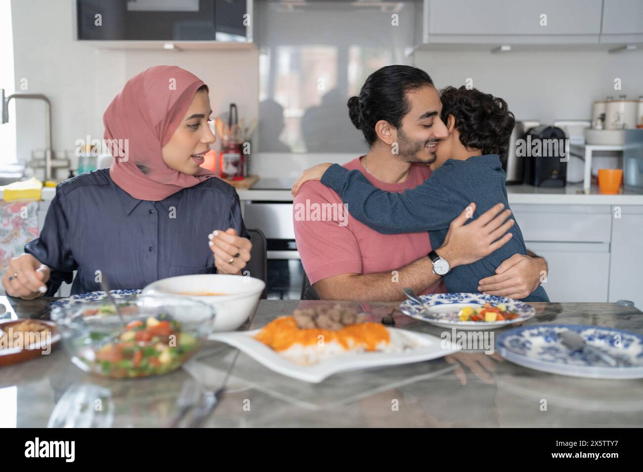 Ragazzo (6-7) abbracciare il padre durante la cena di famiglia Foto Stock