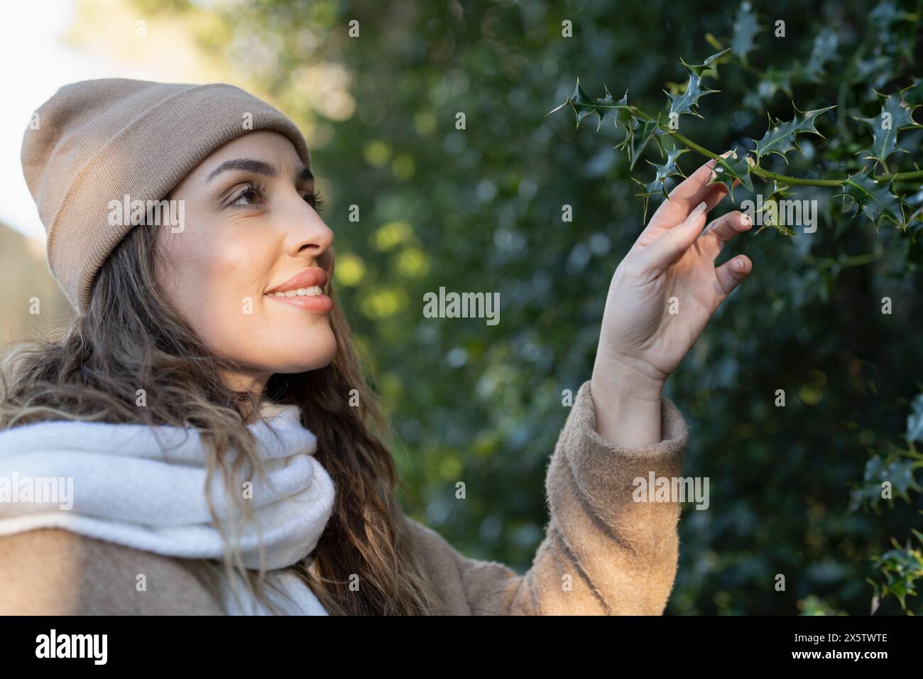 Donna in abbigliamento invernale che tocca foglie di albero Foto Stock