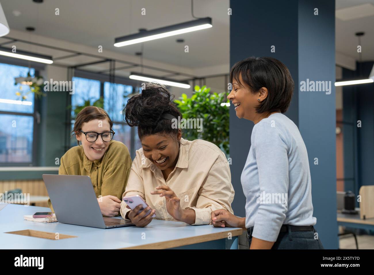 Donne d'affari sorridenti che usano il telefono e il portatile in ufficio Foto Stock