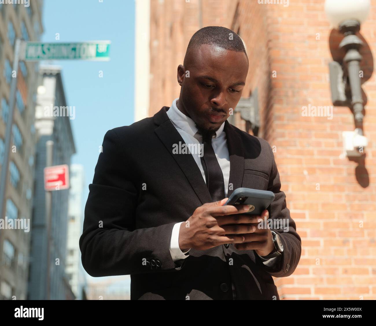 USA, New York City, uomo in tuta che guarda lo smartphone sul marciapiede Foto Stock