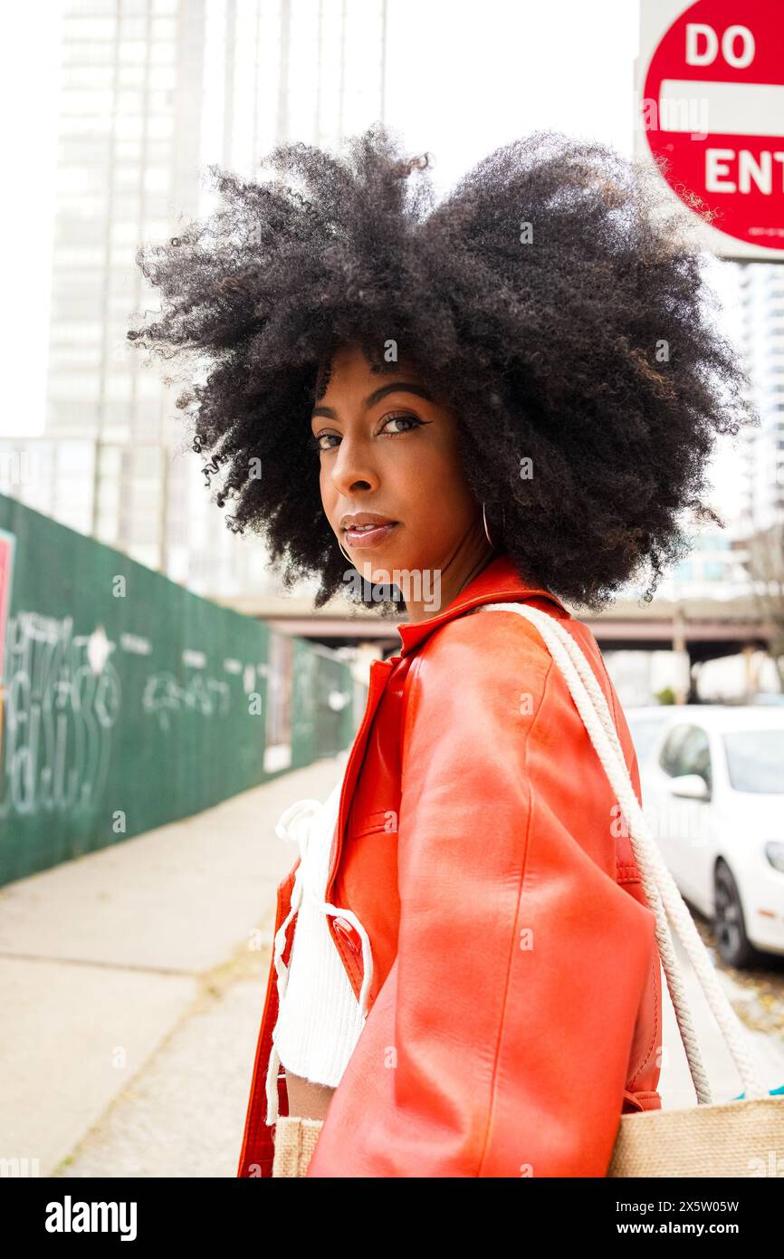 USA, Ritratto di donna con capelli afro che indossa un cappotto di pelle rosso in città Foto Stock