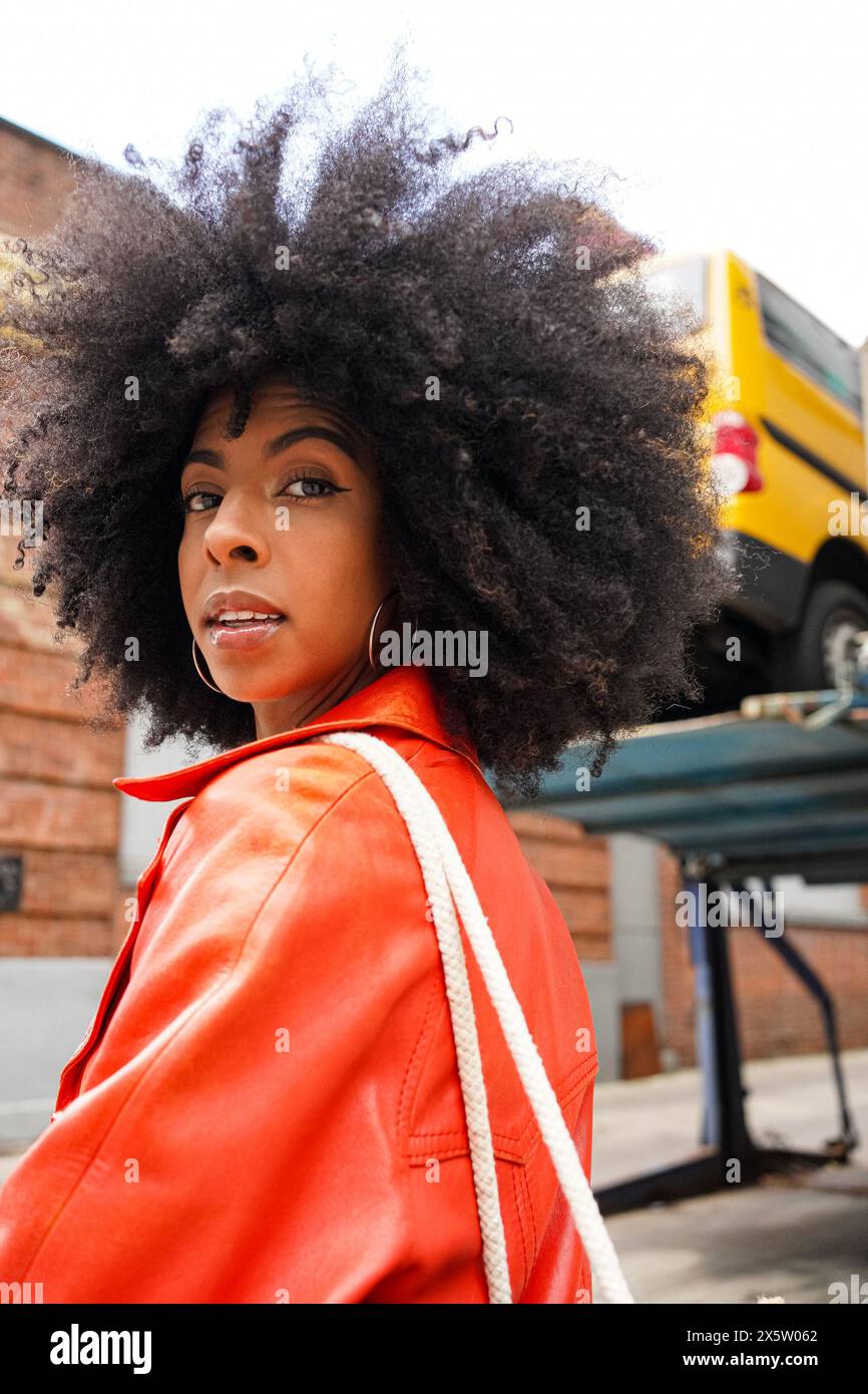 USA, Ritratto di donna con capelli afro che indossa un cappotto di pelle rosso in città Foto Stock