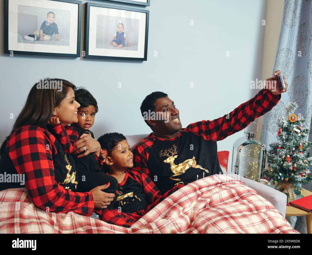 Genitori con figli seduti a letto a fare selfie Foto Stock